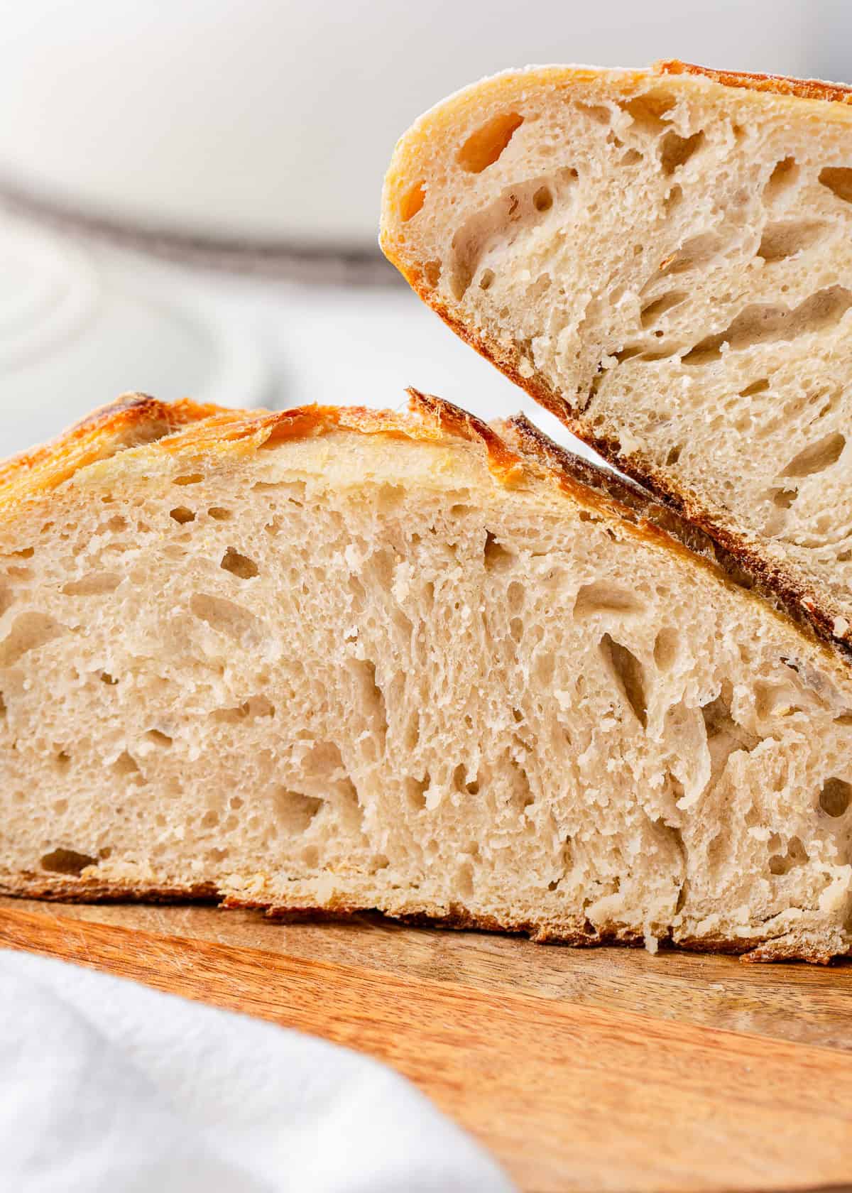 Close-up of same day sourdough bread showing the airy, tender crumb and golden crust, stacked on a wooden cutting board.