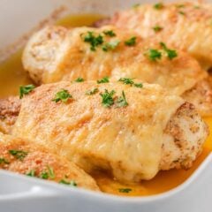 Angled view of Swiss chicken breasts baked in a white dish garnished with parsley.