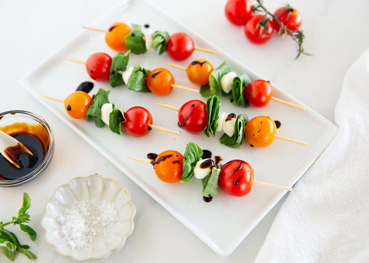 These Caprese skewers are easy and fresh made with cherry tomatoes, mozzarella and basil then drizzled with a balsamic glaze. The perfect summer appetizer! Caprese skewers on a plate.