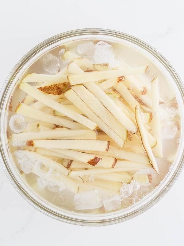 Raw potato strips soaking in an ice water bath to remove excess starch for crispy oven fries.