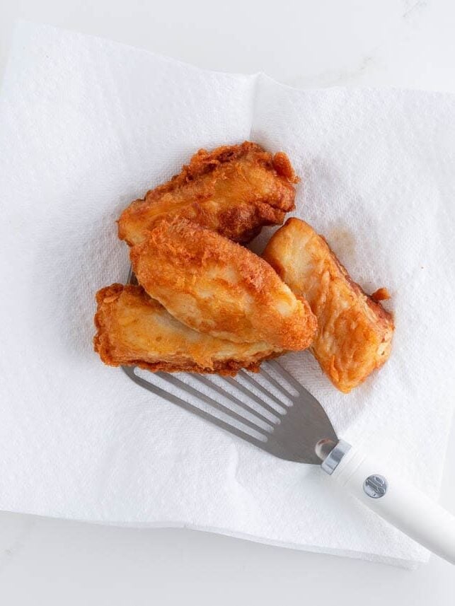 Golden brown battered cod pieces draining on paper towels after frying.