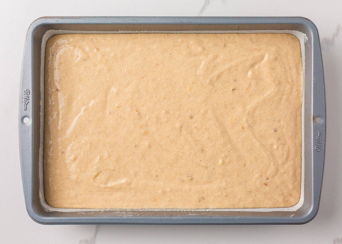 Cake batter evenly spread into a greased baking pan, ready to go in the oven.