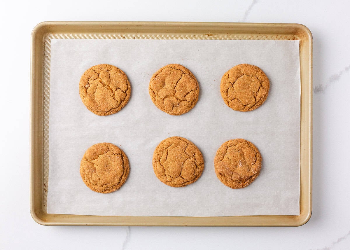 Perfectly spiced and deliciously sweet with the nutty aroma of brown butter, these chewy brown butter pumpkin cookies deliver all the fall coziness in every bite! Six baked brown butter pumpkin cookies cooling on a parchment-lined baking sheet, evenly spaced with golden cracks on top.