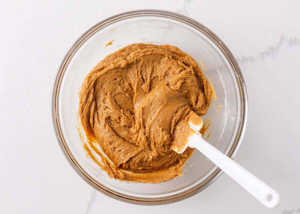 Perfectly spiced and deliciously sweet with the nutty aroma of brown butter, these chewy brown butter pumpkin cookies deliver all the fall coziness in every bite! Browned butter pumpkin cookie dough after mixing, shown in a glass bowl with a white spatula.