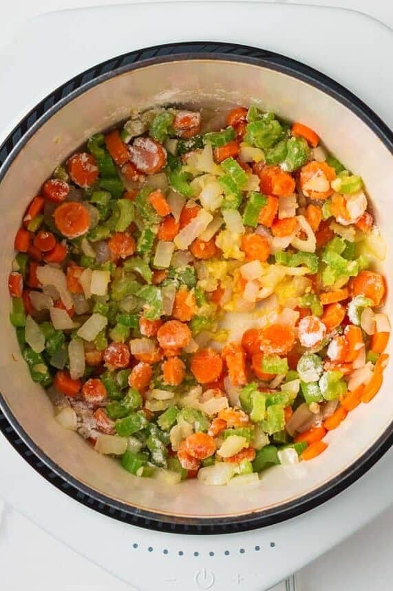Sautéed vegetables including carrots, celery, and onions in a Dutch oven, lightly dusted with flour to form the soup base.