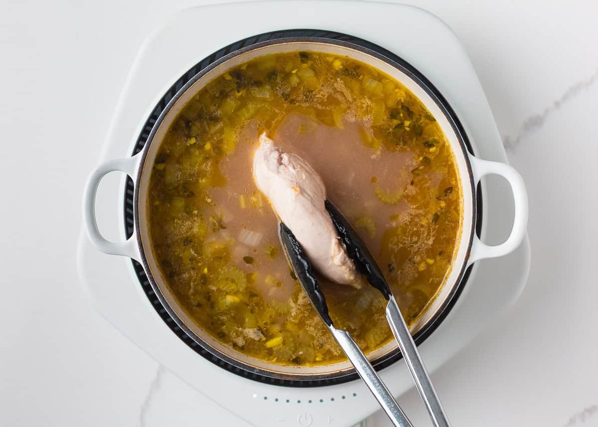 Pulling out cooked chicken breast from a pot of soup to shred.