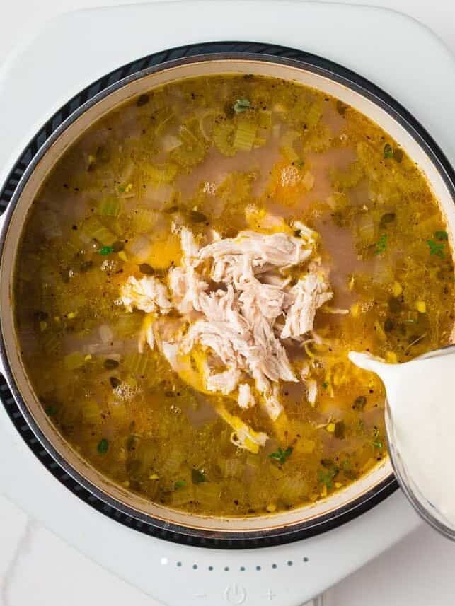 Pouring cream into a pot of shredded chicken and broth to finish the creamy chicken and wild rice soup.