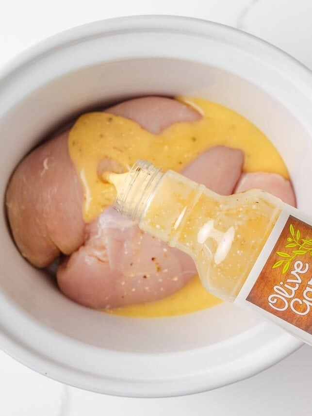 Olive Garden chicken pasta combines tender chicken slow-cooked in a rich, creamy, zesty sauce served over your favorite pasta, for the perfect weeknight meal at home! Pouring Olive Garden Italian dressing over raw chicken breasts in a slow cooker.