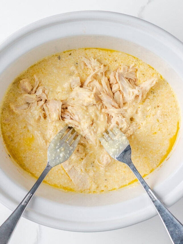 Shredded chicken in creamy sauce inside a slow cooker for crockpot Olive Garden chicken pasta.