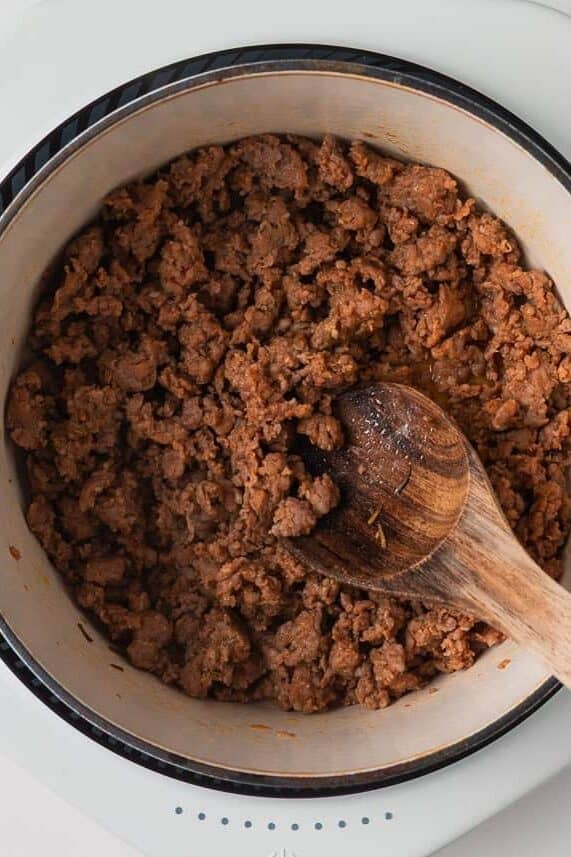 Packed with savory sausage, cheesy tortellini, and spinach in a creamy tomato broth, this Italian sausage tortellini soup is the perfect one-pot meal for a cozy family dinner! Ground Italian sausage browning in a Dutch oven with a wooden spoon.