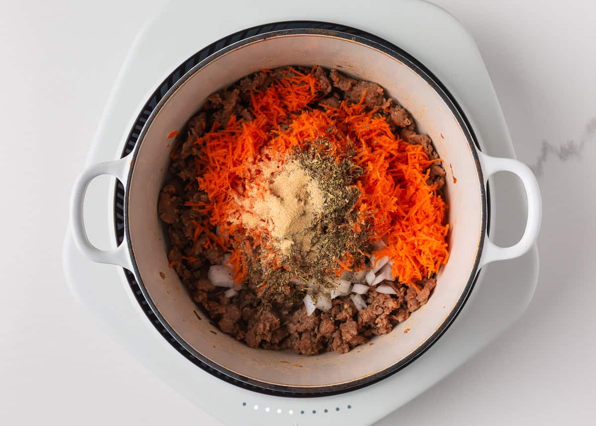 Packed with savory sausage, cheesy tortellini, and spinach in a creamy tomato broth, this Italian sausage tortellini soup is the perfect one-pot meal for a cozy family dinner! Sautéed ground sausage mixed with grated carrots, onions, and seasonings in a white pot.