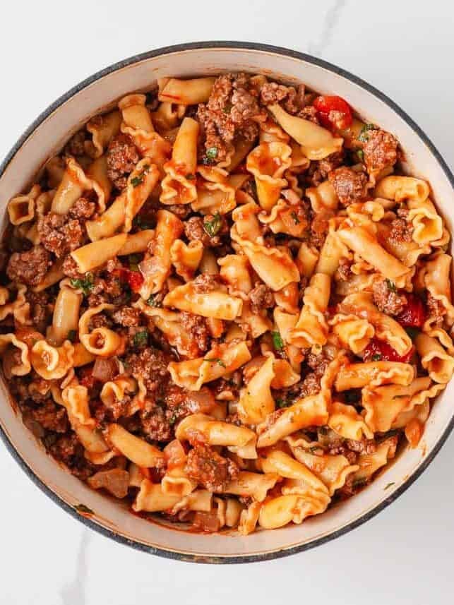 Campanelle pasta combined with meat sauce in a pot to prepare lazy lasagna casserole.