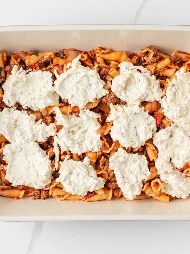 Lazy lasagna casserole layered with campanelle pasta, meat sauce, and dollops of ricotta cheese mixture in a baking dish.