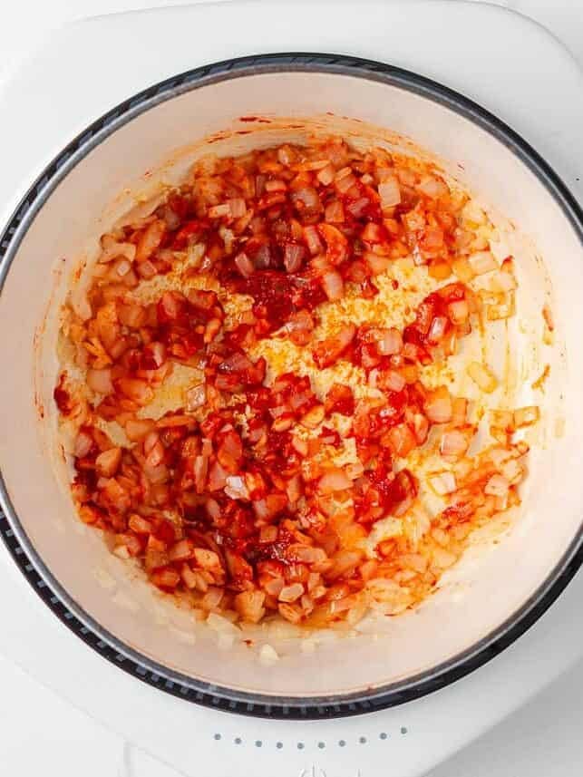 Marry me chicken soup is a cozy spin on the viral marry me chicken recipe made with tender chicken, pasta, sun-dried tomatoes and spinach in a Parmesan cream broth. Step showing sautéed onions and sun-dried tomatoes in a pot before adding broth.