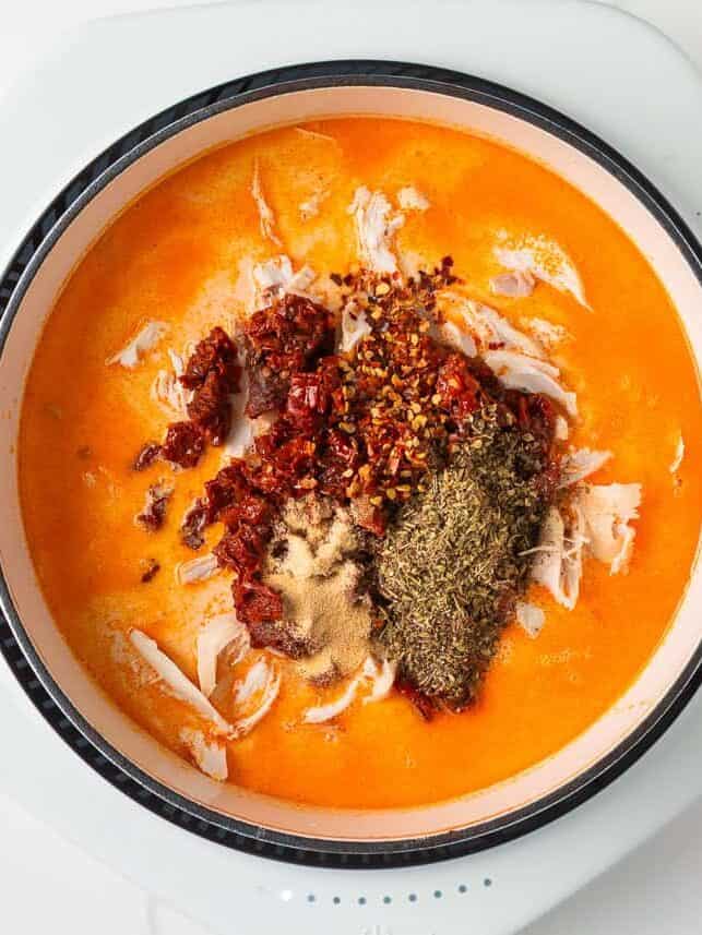 Marry me chicken soup is a cozy spin on the viral marry me chicken recipe made with tender chicken, pasta, sun-dried tomatoes and spinach in a Parmesan cream broth. Step showing chicken, sun-dried tomatoes, and spices added to creamy broth before stirring.