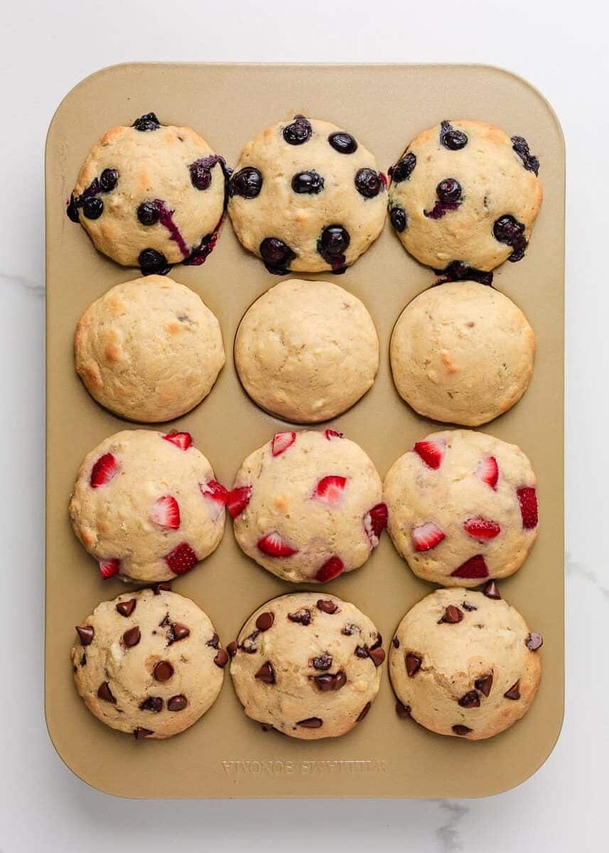 Overhead view of a muffin tin filled with freshly baked pancake muffins topped with blueberries, chopped strawberries, and chocolate chips.