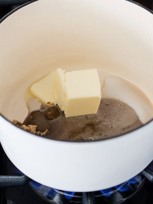 Butter, brown sugar, and cream melting together in a white saucepan over medium heat to start the caramel frosting.
