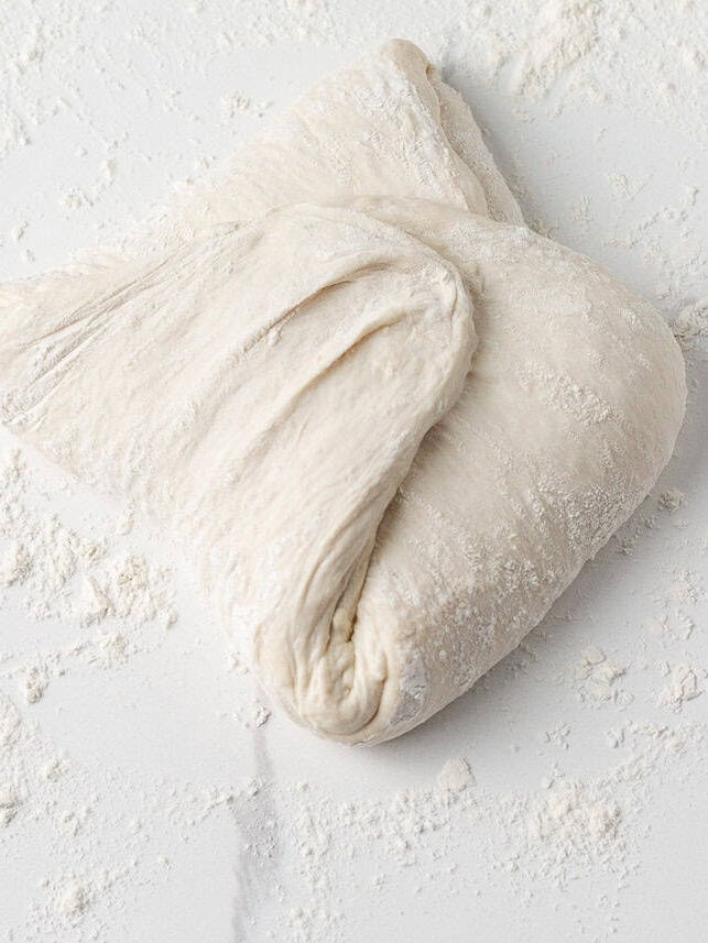 Same day sourdough dough after a series of stretch-and-folds, sitting on a floured surface.
