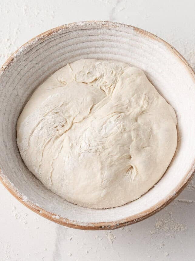 Shaped sourdough dough resting in a floured proofing basket before final rise.