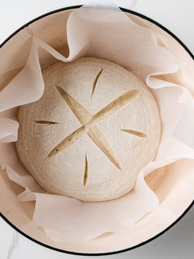 Proofed and scored sourdough dough placed on parchment in a Dutch oven, ready for baking.