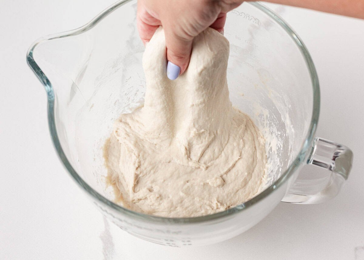 Hand stretching and lifting same day sourdough dough inside a glass mixing bowl to build structure.