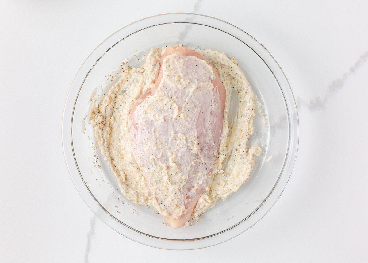 There is nothing better than Swiss chicken bake made with a handful of ingredients and a creamy, cheesy golden topping. Pair with rice and veggies, this easy dinner is served! Raw chicken breast coated in a creamy seasoned mixture in a glass bowl.