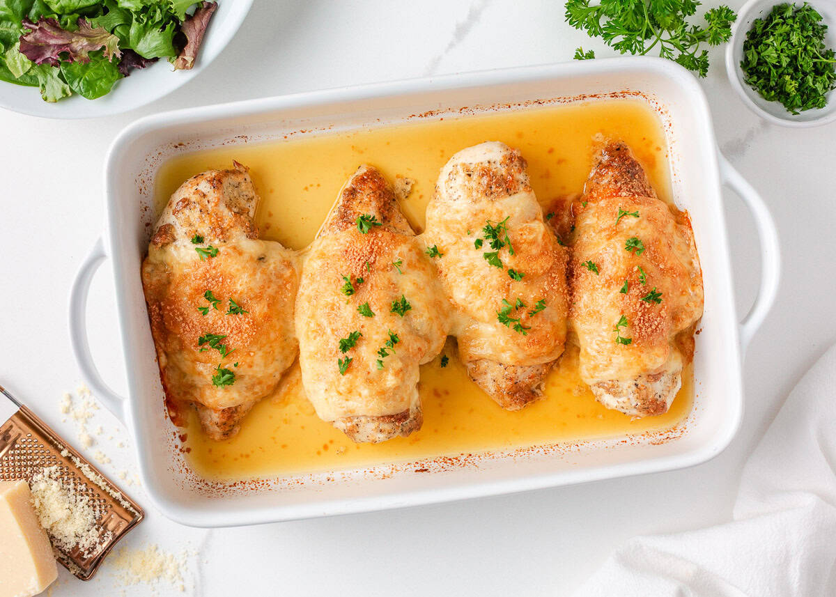 There is nothing better than Swiss chicken bake made with a handful of ingredients and a creamy, cheesy golden topping. Pair with rice and veggies, this easy dinner is served! Four baked Swiss chicken breasts in a casserole dish, covered with melted cheese and garnished with chopped parsley.