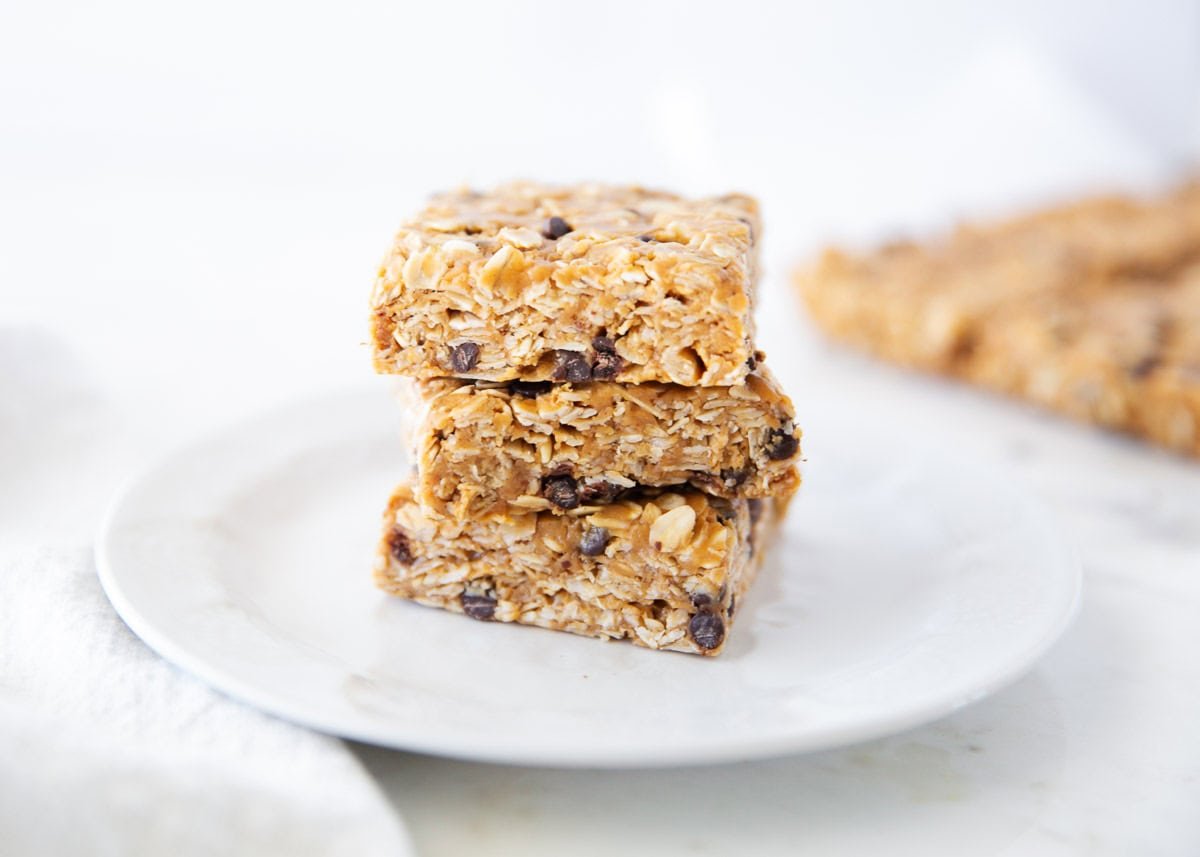 These chewy peanut butter oatmeal bars are an easy no-bake snack, breakfast or healthy dessert made with simple ingredients like peanut butter, oats, and honey! A stack of three no bake peanut butter oatmeal bars on a white plate with visible oats and chocolate chips.