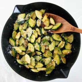Top down photo of saut&eacute;ed zucchini in a skillet cooked until tender and lightly golden, then finished with olive oil, Italian seasoning, and parmesan cheese.