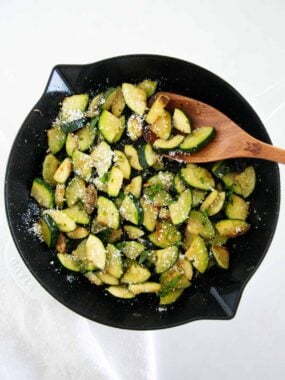 Top down photo of saut&eacute;ed zucchini in a skillet cooked until tender and lightly golden, then finished with olive oil, Italian seasoning, and parmesan cheese.