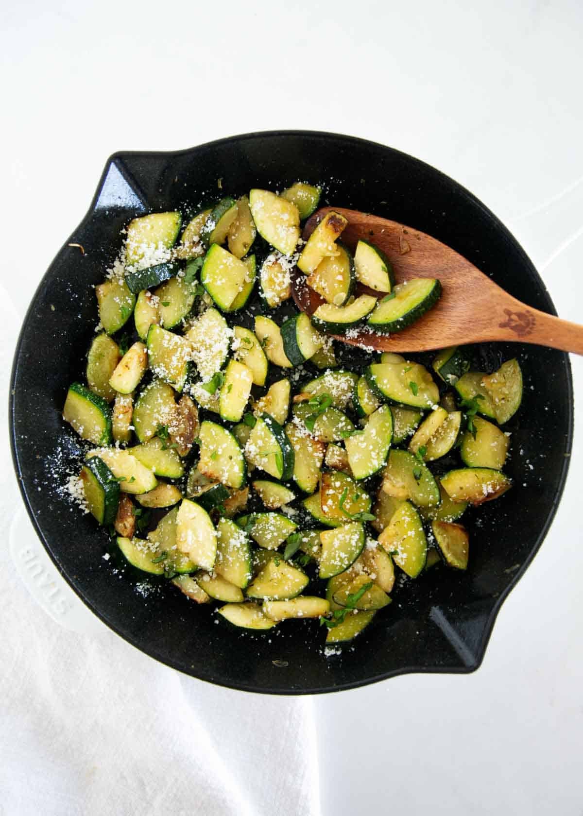 This simple sautéed zucchini is easy to make with a bit of oil, seasoning, and a finish of fresh herbs and Parmesan cheese for the tastiest side dish that the whole family will love! Top down photo of sautéed zucchini in a skillet cooked until tender and lightly golden, then finished with olive oil, Italian seasoning, and parmesan cheese.
