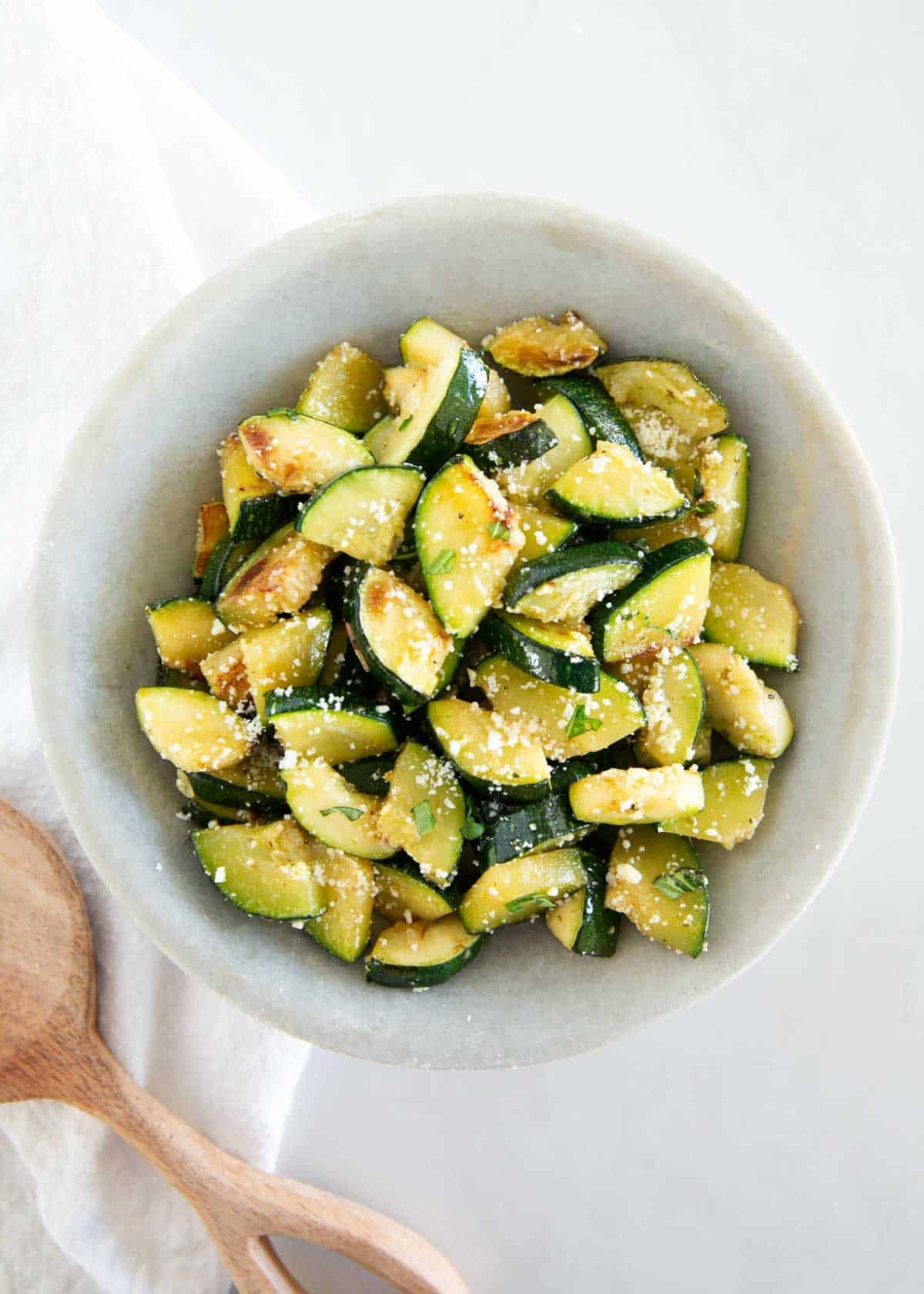 This simple sautéed zucchini is easy to make with a bit of oil, seasoning, and a finish of fresh herbs and Parmesan cheese for the tastiest side dish that the whole family will love! Finished sautéed zucchini served warm with parmesan cheese and herbs in a bowl.