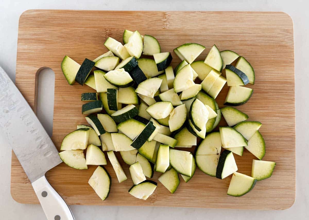 This simple sautéed zucchini is easy to make with a bit of oil, seasoning, and a finish of fresh herbs and Parmesan cheese for the tastiest side dish that the whole family will love! Fresh zucchini chopped into bite sized pieces on a cutting board before cooking.