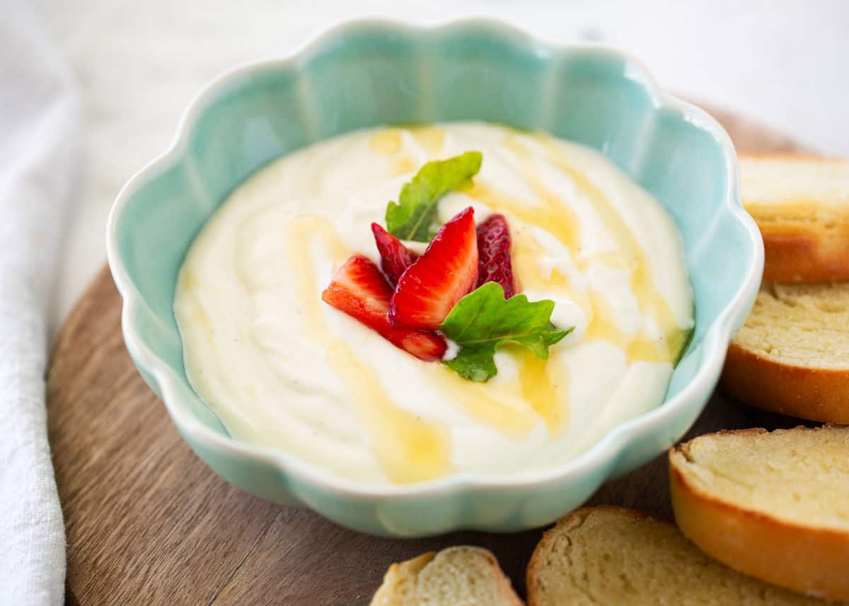 Whipped ricotta dip in a blue bowl topped with a drizzle of honey and strawberries.