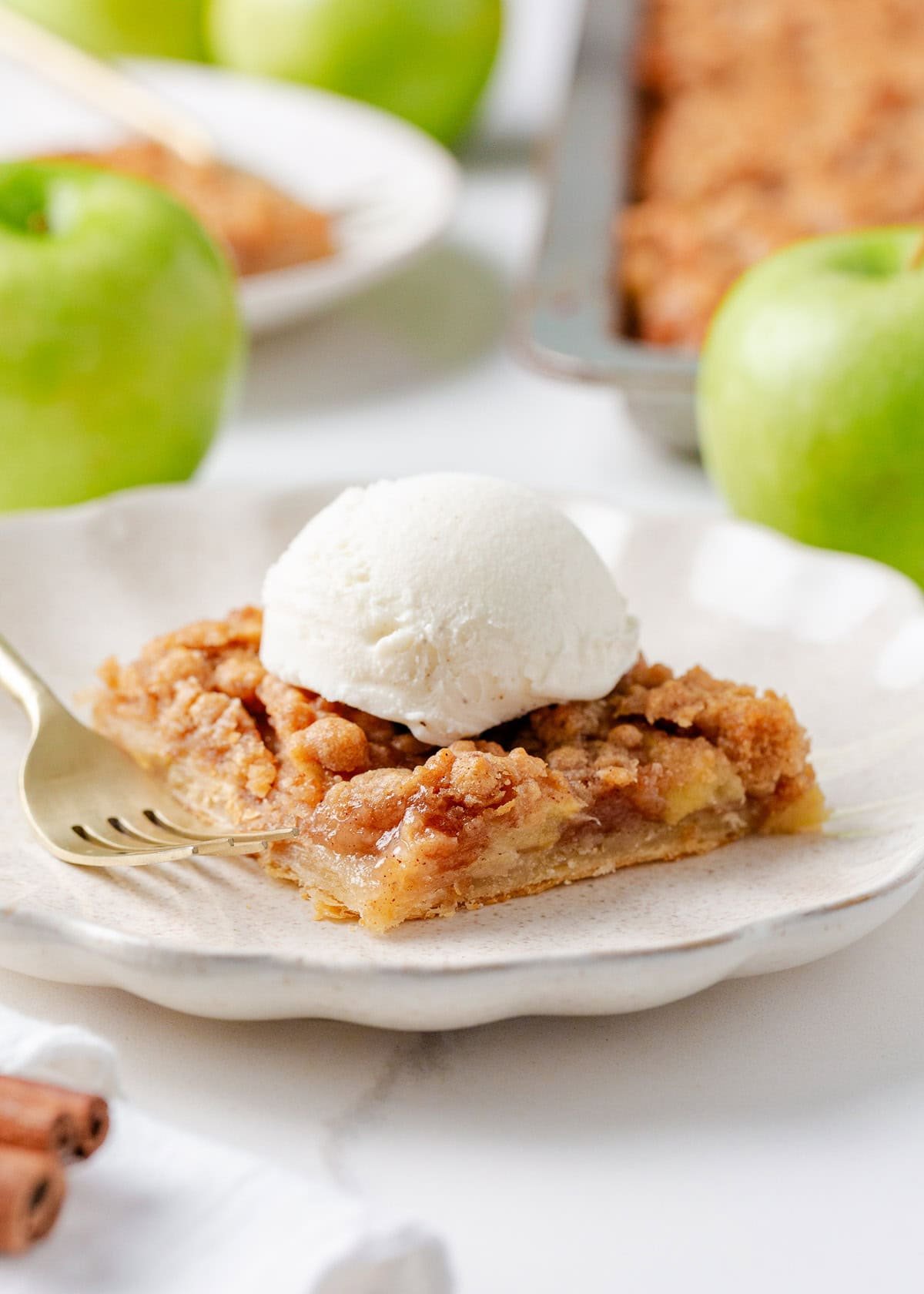 A slice of apple slab pie topped with a scoop of vanilla ice cream on a white plate with a fork.