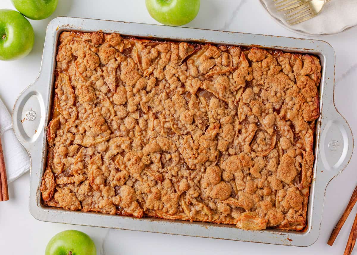 Freshly baked apple slab pie in a rectangular pan with a golden crumb topping.