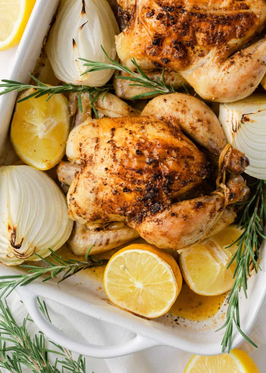 Golden roasted cornish hens with crispy skin served in a white baking dish.