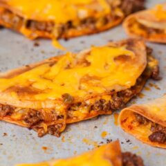 Close-up of crispy sheet pan tacos filled with seasoned ground beef and melted cheddar cheese on a parchment-lined baking sheet.