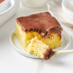 Boston cream poke cake slice on a small plate with forkful of cake showing custard filling.
