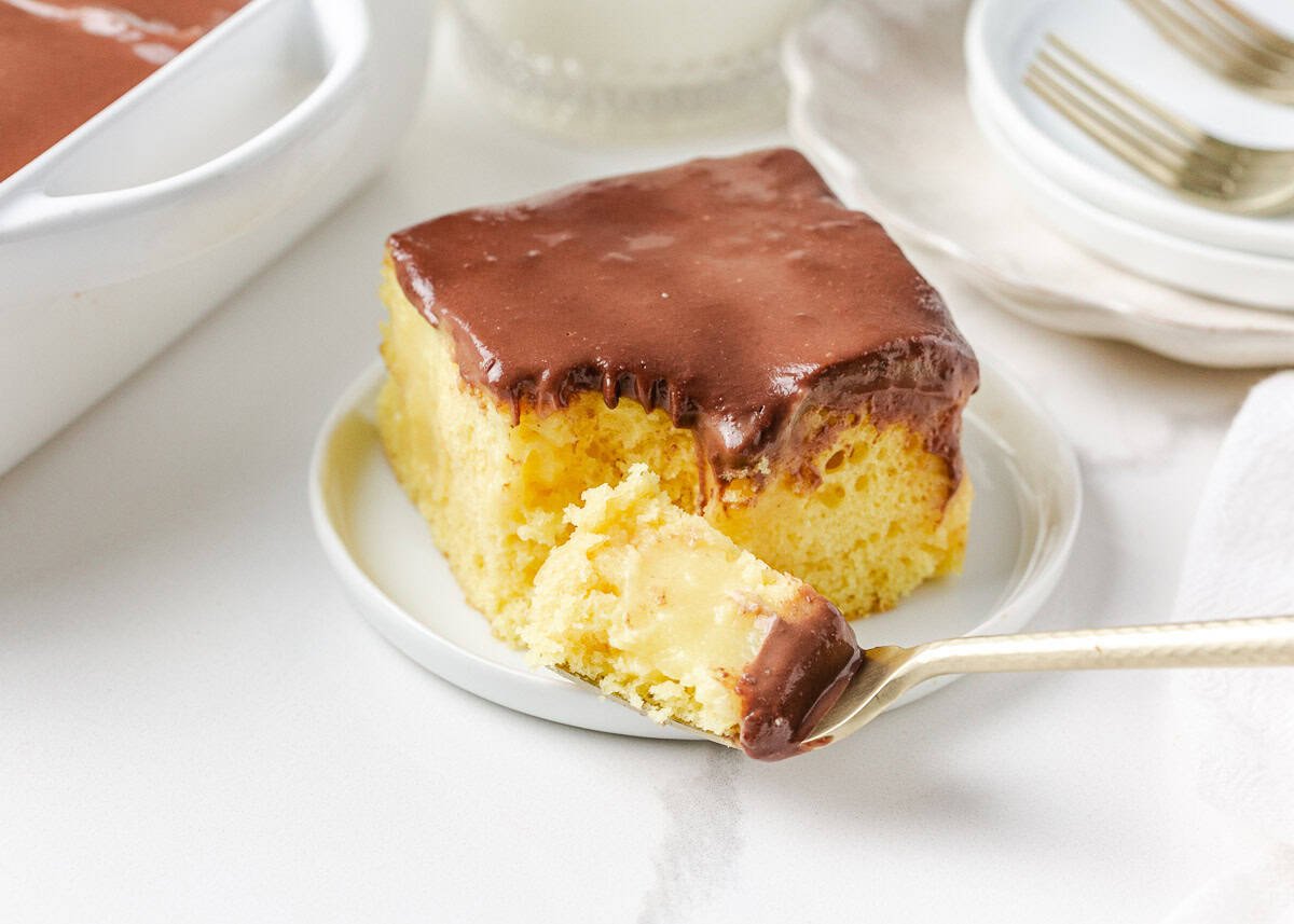 A slice of Boston cream poke cake on a plate with forkful of cake showing custard filling.