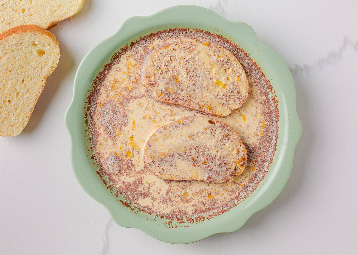 Slices of sourdough bread soaking in egg mixture with cinnamon and milk before cooking.