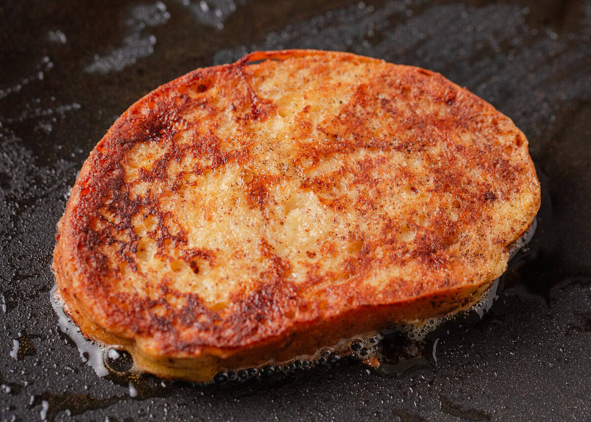 Golden brown slice of sourdough French toast sizzling in butter on a hot griddle.