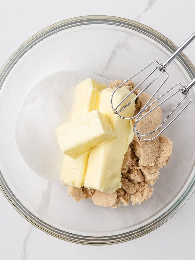 Butter, brown sugar, and granulated sugar in a mixing bowl with a hand mixer, ready to be creamed for Jacque Torres chocolate chip cookies.