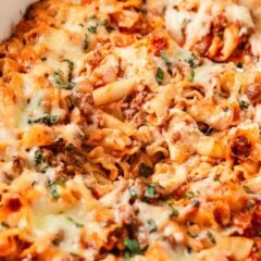 Lasagna casserole with ground beef, pasta, tomato sauce and melted cheese topped with fresh basil in a baking dish.