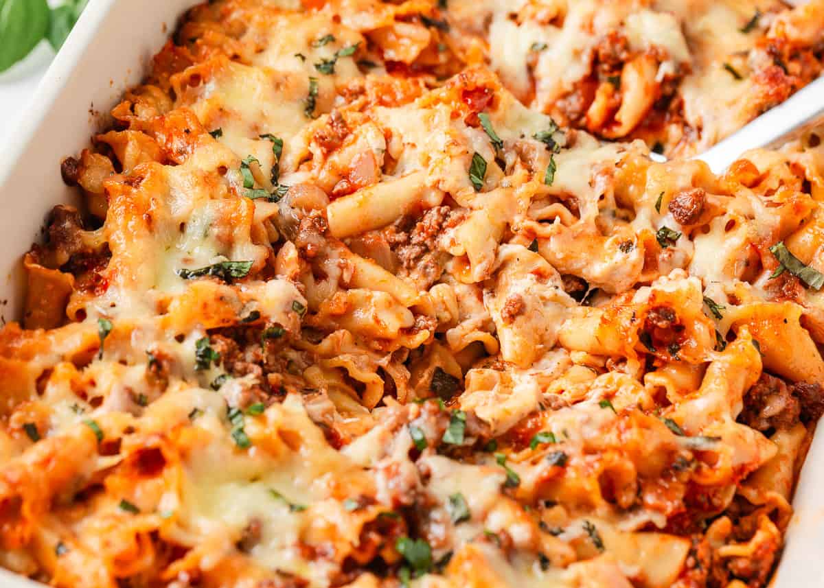 Lasagna casserole with ground beef, pasta, tomato sauce and melted cheese topped with fresh basil in a baking dish.