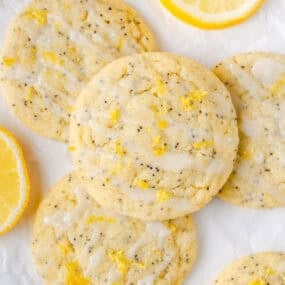 Lemon poppy seed cookies drizzled with glaze and sprinkled with lemon zest, arranged on parchment paper with fresh lemon slices.