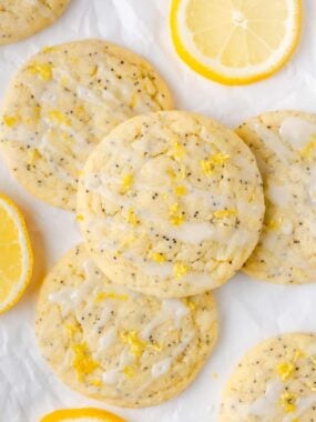 Lemon poppy seed cookies drizzled with glaze and sprinkled with lemon zest, arranged on parchment paper with fresh lemon slices.