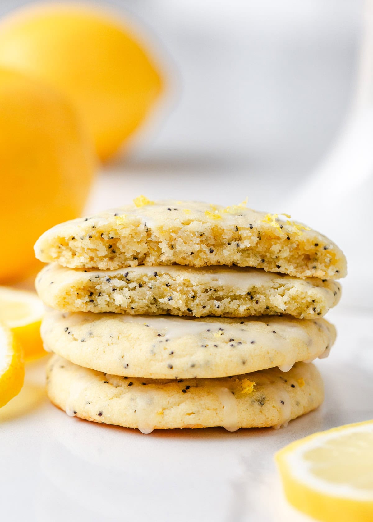 These lemon poppy seed cookies are a no-chill soft, buttery sugar cookie studded with crunchy poppy seeds, infused with sweet citrus flavor, and topped with tangy lemon glaze. Stack of soft lemon poppy seed cookies with glaze and zest, the top cookie showing a moist, fluffy interior with poppy seeds throughout.