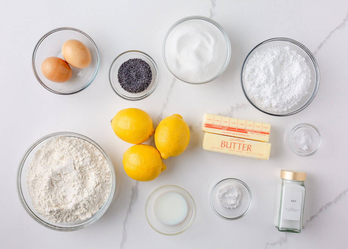 These lemon poppy seed cookies are a no-chill soft, buttery sugar cookie studded with crunchy poppy seeds, infused with sweet citrus flavor, and topped with tangy lemon glaze. Overhead view of lemon poppy seed cookie ingredients, including fresh lemons, flour, sugar, butter, eggs, poppy seeds, and baking powder.