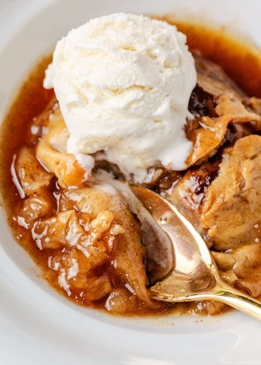Close-up of warm old fashioned apple dumplings topped with vanilla ice cream, served in a bowl with a spoon.